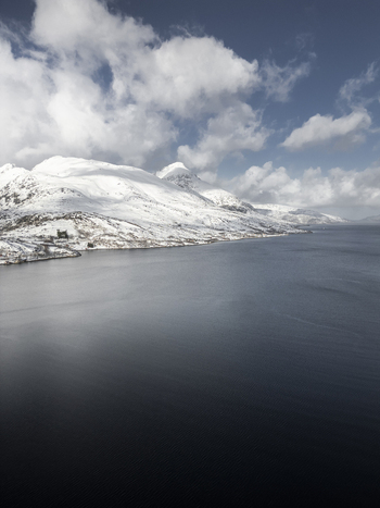 Aerial view of Grotfjord with snow covered mountain peaks and dark blue water under a cloudy sky in Tromvik Troms Norway. Aerial view of Grotfjord with snow covered mountain peaks and dark blue water under a cloudy sky in Tromvik Troms Norway.