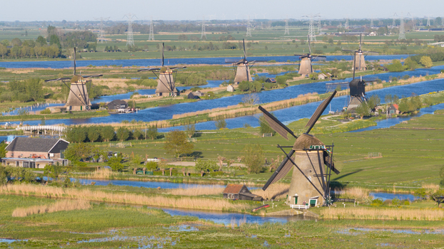 Aerial view of the historic Kinderdijk windmills standing along blue canals surrounded by lush green fields and reeds Kinderdijk South Holland Netherlands. Aerial view of the historic Kinderdijk windmills standing along blue canals surrounded by lush green fields and reeds Kinderdijk South Holland Netherlands.
