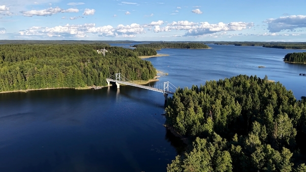 Aerial view of Potkusalmen silta Bridge spanning the blue waters of a lake surrounded by lush green pine forests under a bright sky in Savonlinna Etela Savo Finland. Aerial view of Potkusalmen silta Bridge spanning the blue waters of a lake surrounded by lush green pine forests under a bright sky in Savonlinna Etela Savo Finland.