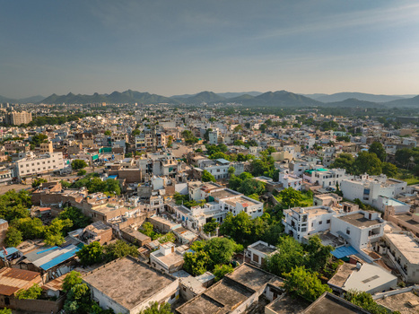 Aerial view of the dense urban landscape of Udaipur with traditional rooftops lush trees and distant mountains under a clear sky in Udaipur Rajasthan India.