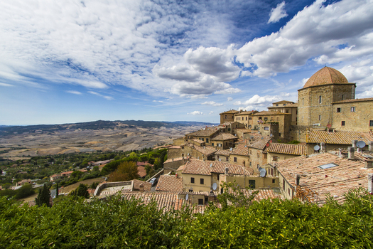 View of sun kissed rooftops cascading down the hillside ancient stone buildings standing proudly against the vibrant blue sky in Volterra Tuscany Italy. View of sun kissed rooftops cascading down the hillside ancient stone buildings standing proudly against the vibrant blue sky in Volterra Tuscany Italy.