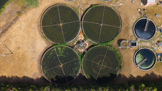 Aerial view of a wastewater treatment works featuring large circular sedimentation tanks surrounded by dry grass and trees in St Neots England United Kingdom. Aerial view of a wastewater treatment works featuring large circular sedimentation tanks surrounded by dry grass and trees in St Neots England United Kingdom.