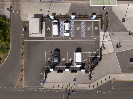 06 May 2026 Aerial view of an electric vehicle charging station with cars parked in designated bays and pedestrians walking on the sidewalk. 06 May 2026 Aerial view of an electric vehicle charging station with cars parked in designated bays and pedestrians walking on the sidewalk.