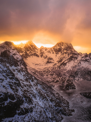 Aerial view of snow capped mountains kissed by the golden glow of sunrise contrasting sharply with the icy waters below Leknes Nordland Norway.
