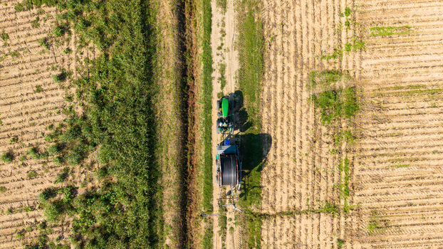 Aerial view of a green tractor pulling a reel irrigation system across a cultivated agricultural field in the countryside in Bettola Zeloforomagno Lombardy Italy. Aerial view of a green tractor pulling a reel irrigation system across a cultivated agricultural field in the countryside in Bettola Zeloforomagno Lombardy Italy.