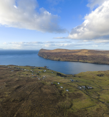 Aerial view of the coastal village with scattered houses along the rugged cliffs and deep blue waters of the loch under a cloudy sky in Milovaig Scotland United Kingdom.