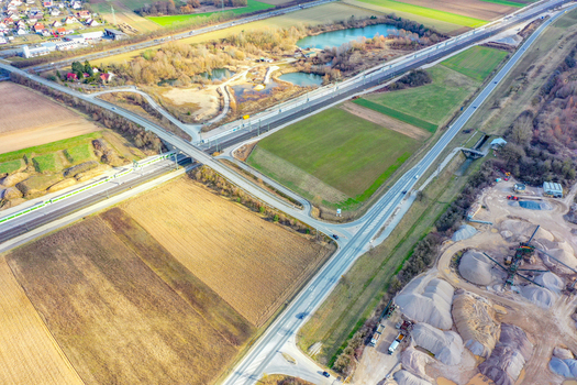 Aerial view of the landscape featuring a highway railway tracks and small ponds near a construction site and green fields in Buttenheim Bavaria Germany. Aerial view of the landscape featuring a highway railway tracks and small ponds near a construction site and green fields in Buttenheim Bavaria Germany.