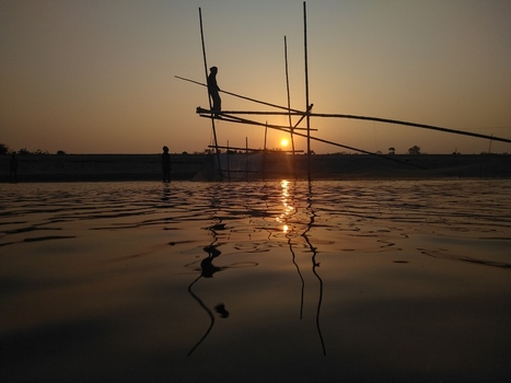 View of a fisherman standing on a bamboo fishing structure in the river at sunset in Kushtia Khulna Division Bangladesh. View of a fisherman standing on a bamboo fishing structure in the river at sunset in Kushtia Khulna Division Bangladesh.