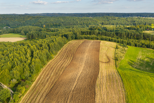 Aerial view of the Kashubia region featuring plowed brown soil and vibrant green agricultural fields surrounded by dense forest under a clear sky in Pomeranian Voivodeship Poland. Aerial view of the Kashubia region featuring plowed brown soil and vibrant green agricultural fields surrounded by dense forest under a clear sky in Pomeranian Voivodeship Poland.