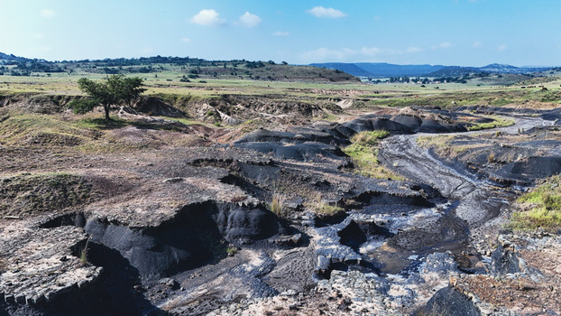 Aerial view of eroded dark earth formations and a lone tree in a rural landscape with rolling green hills under a blue sky in Pietermaritzburg KwaZulu Natal South Africa.