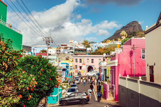 View of brightly colored houses in the Bo Kaap neighborhood with people walking on the street and Lion s Head mountain in the background Cape Town Western Cape South Africa. View of brightly colored houses in the Bo Kaap neighborhood with people walking on the street and Lion s Head mountain in the background Cape Town Western Cape South Africa.
