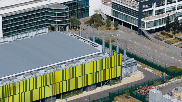 Aerial view of the Kao Data campus featuring modern industrial architecture with green and yellow facade panels ventilation systems and paved areas in Harlow England United Kingdom. Aerial view of the Kao Data campus featuring modern industrial architecture with green and yellow facade panels ventilation systems and paved areas in Harlow England United Kingdom.