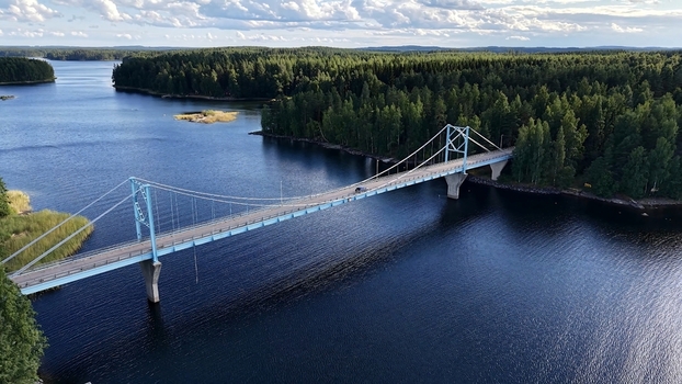 Aerial view of Potkusalmen silta Bridge spanning over the deep blue waters of a lake surrounded by dense pine forests under a bright sky in Savonlinna Etela Savo Finland. Aerial view of Potkusalmen silta Bridge spanning over the deep blue waters of a lake surrounded by dense pine forests under a bright sky in Savonlinna Etela Savo Finland.