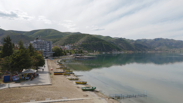 Aerial view of the Lake Ohrid shoreline in Pogradec with small wooden boats on the sand a lakeside promenade and mountains in the background in Pogradec Korce County Albania. Aerial view of the Lake Ohrid shoreline in Pogradec with small wooden boats on the sand a lakeside promenade and mountains in the background in Pogradec Korce County Albania.