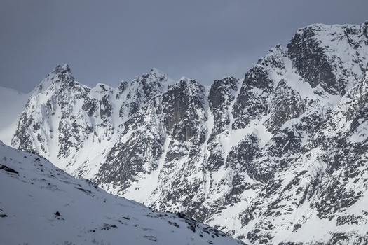 View of snow covered jagged mountain peaks and steep rocky ridges under an overcast sky in Ersfjord Troms Norway. View of snow covered jagged mountain peaks and steep rocky ridges under an overcast sky in Ersfjord Troms Norway.
