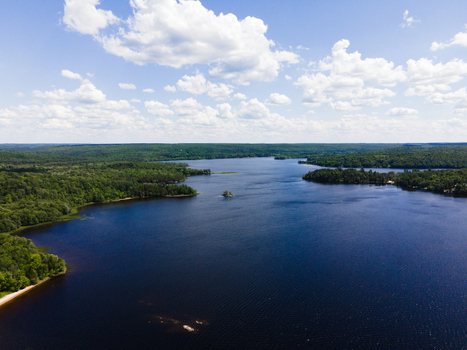 Aerial view of Commanda Lake surrounded by dense green forests under a bright blue sky with scattered white clouds in Restoule Ontario Canada. Aerial view of Commanda Lake surrounded by dense green forests under a bright blue sky with scattered white clouds in Restoule Ontario Canada.