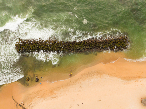 Aerial view of Dadalla beach featuring a stone breakwater with waves crashing against the rocks and people swimming in the clear water in Galle Southern Province Sri Lanka. Aerial view of Dadalla beach featuring a stone breakwater with waves crashing against the rocks and people swimming in the clear water in Galle Southern Province Sri Lanka.