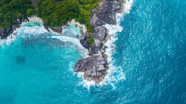 Aerial view of the coastline near Anse Soleil Beachcomber Hotel with turquoise waters crashing against granite rocks and lush tropical vegetation in Mahe Baie Lazare Seychelles.