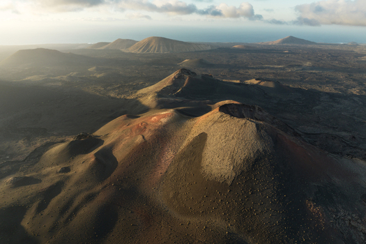 Aerial view of volcanic craters and vast lava fields under a soft morning light with scattered clouds in Lanzarote Canarias Spain. Aerial view of volcanic craters and vast lava fields under a soft morning light with scattered clouds in Lanzarote Canarias Spain.