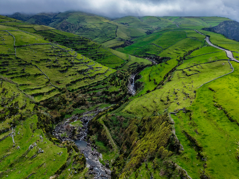 Aerial view of vibrant green hills cascading down to a rocky riverbed framed by a winding road under a cloudy sky Flores A&ccedil;ores Portugal.