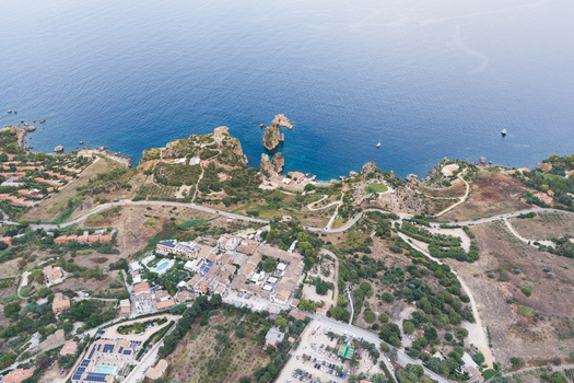 Aerial view of the rugged coastline and rocky cliffs of Riserva Naturale Orientata dello Zingaro with Mediterranean sea winding roads and buildings in San Vito Lo Capo Sicilia Italy. Aerial view of the rugged coastline and rocky cliffs of Riserva Naturale Orientata dello Zingaro with Mediterranean sea winding roads and buildings in San Vito Lo Capo Sicilia Italy.