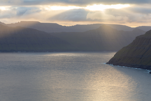View of the dramatic coastal landscape of the Faroe Islands with steep mountains rising from the sea under a cloudy sky with sunbeams breaking through Faroe Islands. View of the dramatic coastal landscape of the Faroe Islands with steep mountains rising from the sea under a cloudy sky with sunbeams breaking through Faroe Islands.
