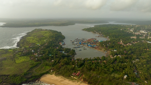 Aerial view of the coastal harbor in Devgad featuring numerous fishing boats lush green hills and the distant Devgad Windmills under a cloudy sky in Devgad Maharashtra India. Aerial view of the coastal harbor in Devgad featuring numerous fishing boats lush green hills and the distant Devgad Windmills under a cloudy sky in Devgad Maharashtra India.