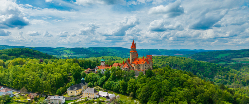 Aerial view of Bouzov Castle with its iconic red roofed towers nestled among dense green forests and rolling hills under a cloudy sky in Bouzov Olomoucky kraj Czechia. Aerial view of Bouzov Castle with its iconic red roofed towers nestled among dense green forests and rolling hills under a cloudy sky in Bouzov Olomoucky kraj Czechia.