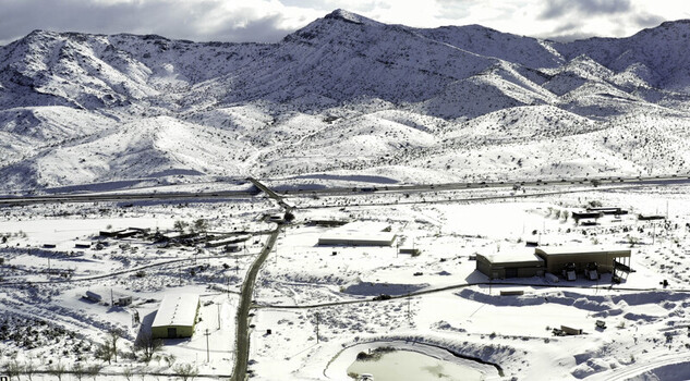 Aerial view of snow covered mountains surrounding the desert landscape and industrial buildings in Lancaster CA United States.