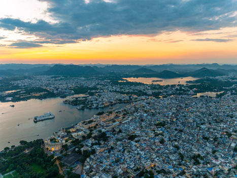 Aerial view of the historic city of Udaipur with its iconic palaces dense urban rooftops and shimmering lakes under a golden sunset sky in Udaipur Rajasthan India.