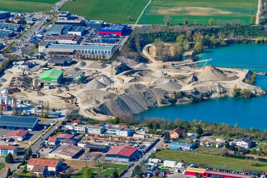 Aerial view of an industrial landscape where piles of sand and gravel meet the serene blue of a quarry lake creating a stark contrast Sausheim Grand Est France.