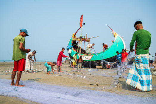 Teknaf Bangladesh 10 March 2026 View of fishermen haul in their nets the vibrant turquoise boat contrasting against the soft sandy shore.