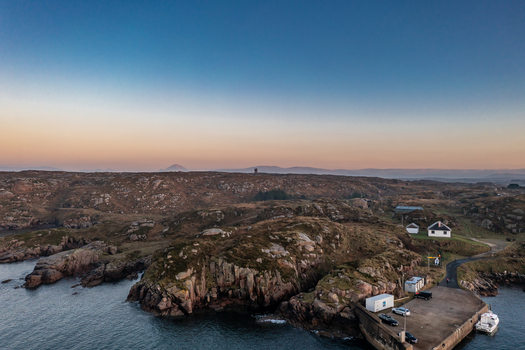 Aerial view of the rugged coastline and harbor with rocky terrain small white buildings and calm waters under a soft sunset sky in Kincasslagh County Donegal Ireland. Aerial view of the rugged coastline and harbor with rocky terrain small white buildings and calm waters under a soft sunset sky in Kincasslagh County Donegal Ireland.