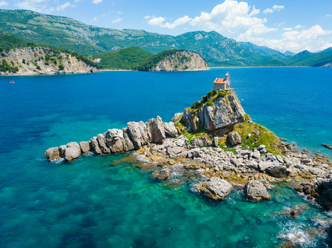 Aerial view of St. Nedjelja Church perched on a rocky islet surrounded by turquoise Adriatic Sea waters and rugged mountains in Petrovac Montenegro. Aerial view of St. Nedjelja Church perched on a rocky islet surrounded by turquoise Adriatic Sea waters and rugged mountains in Petrovac Montenegro.