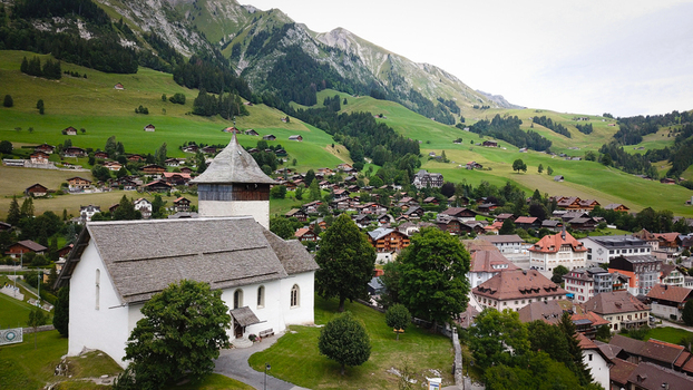 Aerial view of the Temple de Chateau d Oex and traditional wooden chalets nestled in the lush green valley of the Swiss Alps Chateau d Oex Vaud Switzerland. Aerial view of the Temple de Chateau d Oex and traditional wooden chalets nestled in the lush green valley of the Swiss Alps Chateau d Oex Vaud Switzerland.
