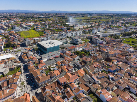 Aerial view of a vibrant urban tapestry woven with ancient terracotta roofs and a striking modern teal structure bathed in the bright Portuguese sun Ilhavo Aveiro Portugal. Aerial view of a vibrant urban tapestry woven with ancient terracotta roofs and a striking modern teal structure bathed in the bright Portuguese sun Ilhavo Aveiro Portugal.