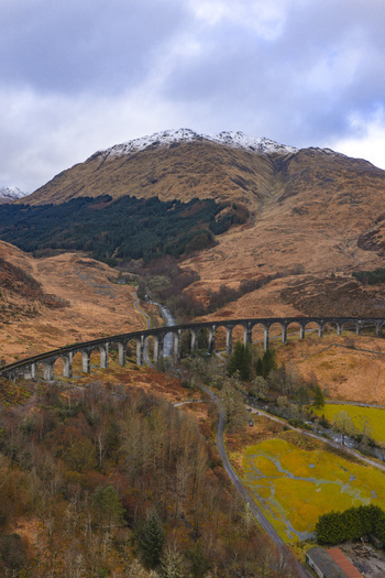 Aerial view of the Glenfinnan Viaduct with its curved stone arches set against snow capped mountains and a winding river in the valley Glenfinnan Scotland United Kingdom.