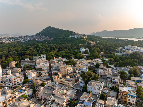 Aerial view of the historic city of Udaipur with its dense urban landscape traditional rooftops and lush green hills under a soft sunset sky in Udaipur Rajasthan India. Aerial view of the historic city of Udaipur with its dense urban landscape traditional rooftops and lush green hills under a soft sunset sky in Udaipur Rajasthan India.