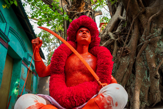 Munshiganj Bangladesh 13 April 2026 View of a man painted in red holding a sword during a traditional festival in front of a banyan tree.