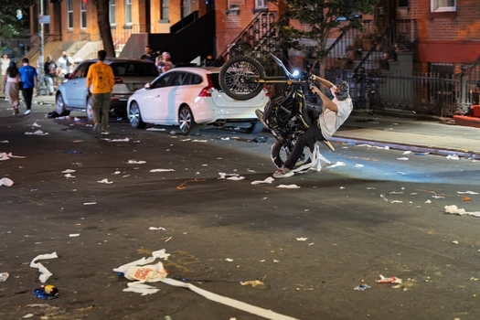 Williamsburg New York USA 14 June 2026 View of a person performing a wheelie on a motorcycle on a street covered in debris during a celebration. Williamsburg New York USA 14 June 2026 View of a person performing a wheelie on a motorcycle on a street covered in debris during a celebration.