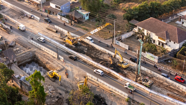 Indonesia 24 September 2026 Aerial view of road construction site with heavy machinery excavators and cranes operating alongside traffic on a busy road in Indonesia.