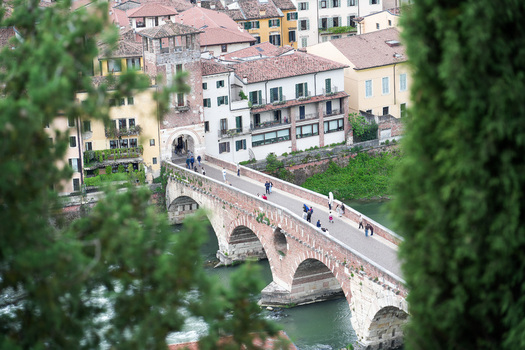 Aerial view of Ponte Pietra bridge with people walking across the Adige river surrounded by historic buildings and lush greenery Verona Veneto Italy.