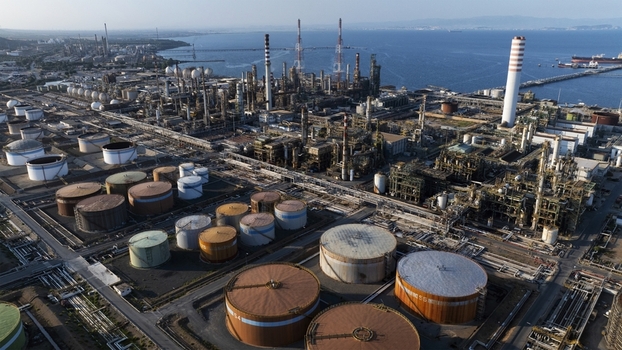 Aerial view of a large industrial oil refinery complex with storage tanks tall chimneys and pipelines along the coast under a clear sky in Cagliari Sardinia Italy. Aerial view of a large industrial oil refinery complex with storage tanks tall chimneys and pipelines along the coast under a clear sky in Cagliari Sardinia Italy.