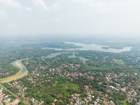 Aerial view of the winding Hikkaduwa Lake surrounded by dense tropical vegetation and residential houses under a hazy sky in Hikkaduwa Southern Province Sri Lanka. Aerial view of the winding Hikkaduwa Lake surrounded by dense tropical vegetation and residential houses under a hazy sky in Hikkaduwa Southern Province Sri Lanka.