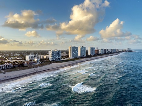 Aerial view of Deerfield Beach featuring high rise condominiums along the sandy coastline with turquoise ocean waves and a bright blue sky in Deerfield Beach Florida United States. Aerial view of Deerfield Beach featuring high rise condominiums along the sandy coastline with turquoise ocean waves and a bright blue sky in Deerfield Beach Florida United States.