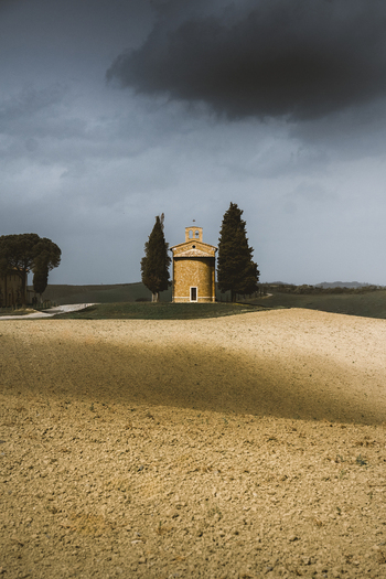 View of a small church surrounded by picturesque fields and trees under a cloudy sky Pienza Italy.