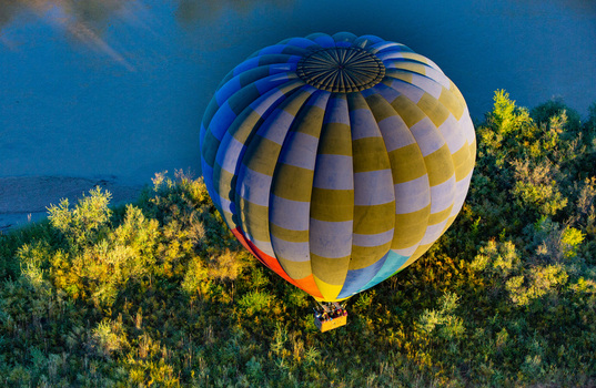Albuquerque United States 11 October 2017 View of a vibrant hot air balloon ascends over a lush canopy of green trees the blue sky contrasting with the balloon s colorful stripes.. Albuquerque United States 11 October 2017 View of a vibrant hot air balloon ascends over a lush canopy of green trees the blue sky contrasting with the balloon s colorful stripes..