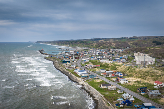 Aerial view of the coastal town of Wakkanai with houses a winding road and rugged shoreline along the Sea of Japan in Wakkanai Hokkaido Japan.
