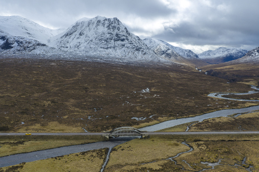 Aerial view of the River Etive Bridge crossing a winding river with snow capped mountains and a yellow car on the road in Ballachulish Scotland United Kingdom. Aerial view of the River Etive Bridge crossing a winding river with snow capped mountains and a yellow car on the road in Ballachulish Scotland United Kingdom.