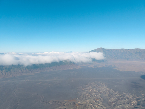 Aerial view of Mount Bromo with volcanic landscape sand sea and low hanging clouds under a clear blue sky in Tosari East Java Indonesia.